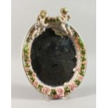 A MEISSEN STYLE OVAL WALL MIRROR, encrusted with cherubs and flowers. 12ins high.