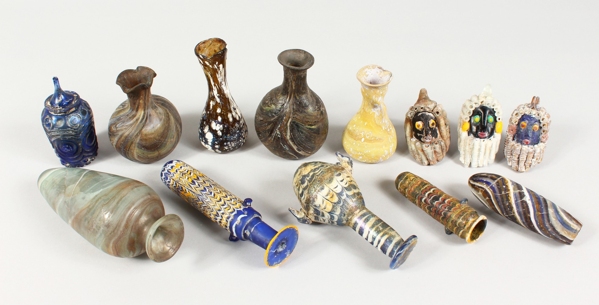 A GROUP OF THIRTEEN ROMAN GLASS BOTTLES AND JARS, including three tops in the form of heads (13).