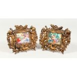 A PAIR OF CAST BRONZE CHERUB FRAMES, containing classical porcelain plaques. 7ins wide.