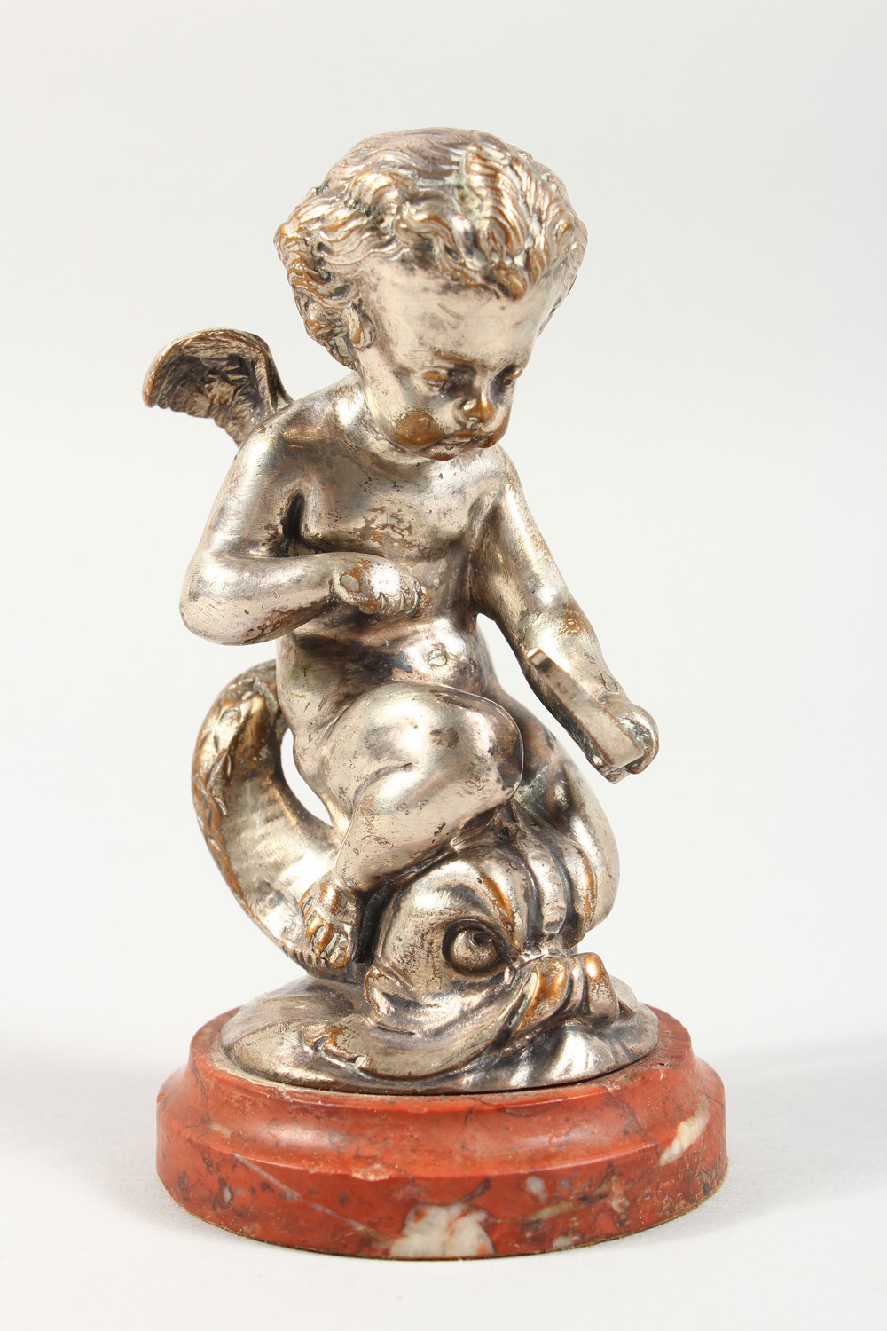 A SILVERED CAST METAL MODEL OF CUPID RIDING ON A DOLPHIN, on a marble base. 5ins high overall.
