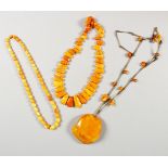 THREE CHINESE EGG YOLK AMBER NECKLACES, one with metal links, and a large carved pendant 34cm, one