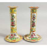 A GOOD PAIR OF CANTON FAMILLE JAUNE CANDLESTICKS with panels of flowers and birds. 7ins high.