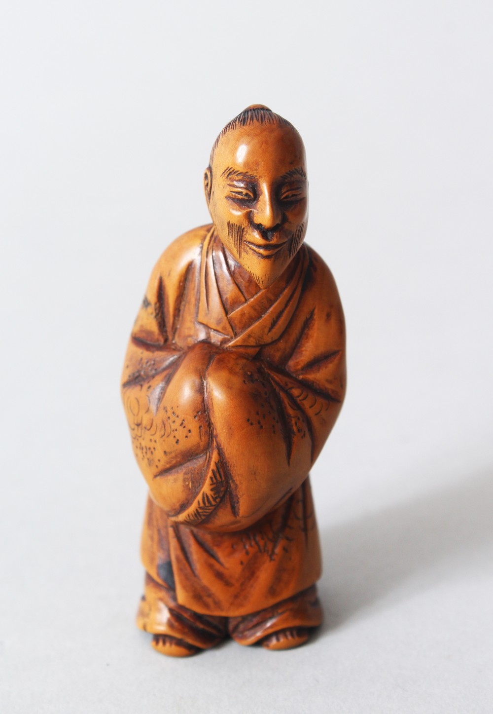 A JAPANESE MEIJI PERIOD CARVED WOODEN NETSUKE OF A CHINESE LITERATUS, stood holding his hands