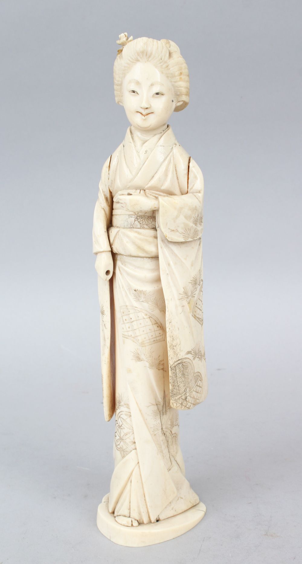 A JAPANESE MEIJI PERIOD CARVED IVORY OKIMONO OF A GEISHA GIRL, the lady stood holding some