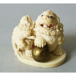 A JAPANESE MEIJI PERIOD CARVED IVORY NETSUKE OF SHI SHI DOGS, the larger shi shi with its paw upon a