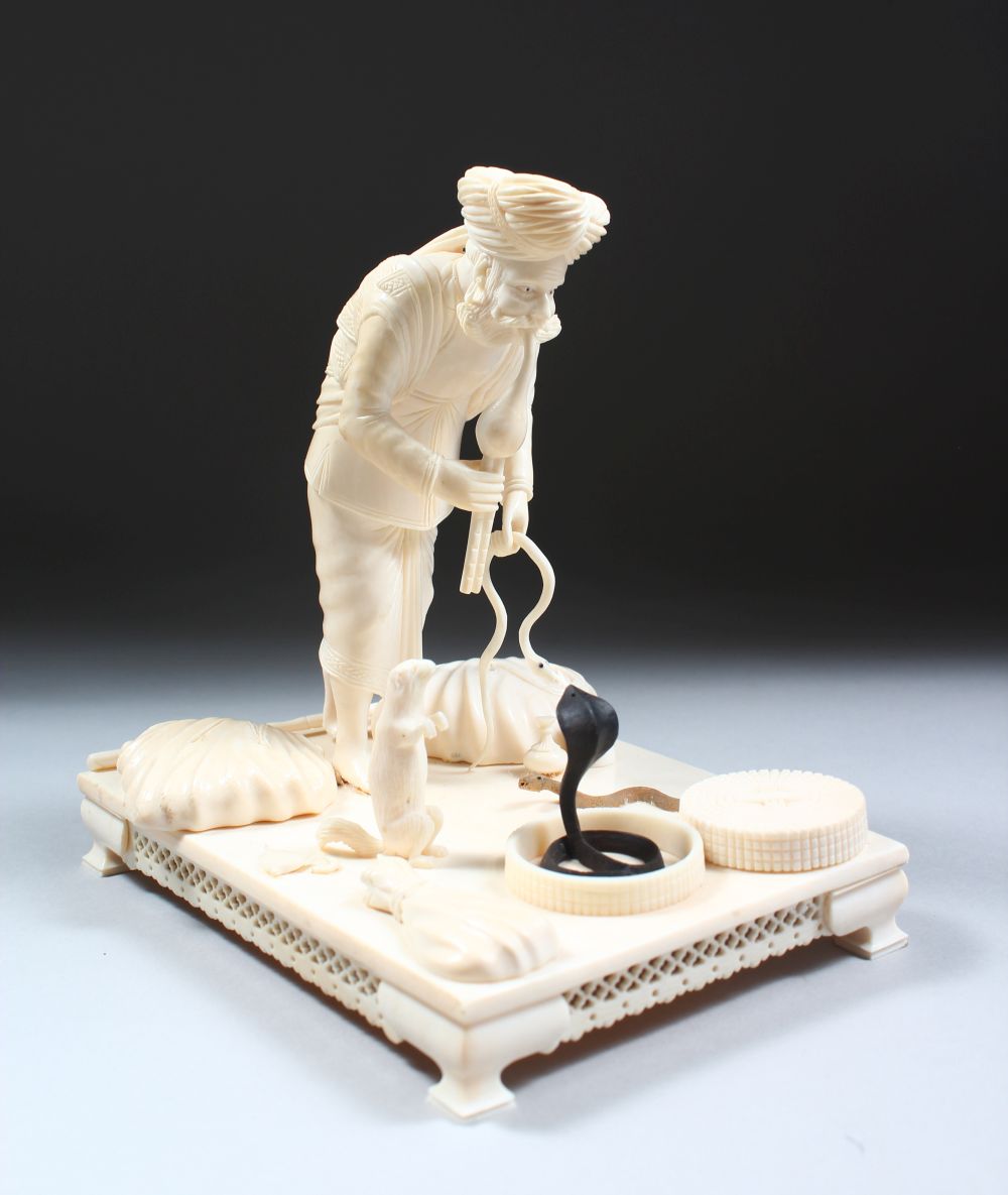 A 19TH CENTURY CARVED INDIAN IVORY MODEL OF A SNAKE CHARMER, the man stood over two snakes with a