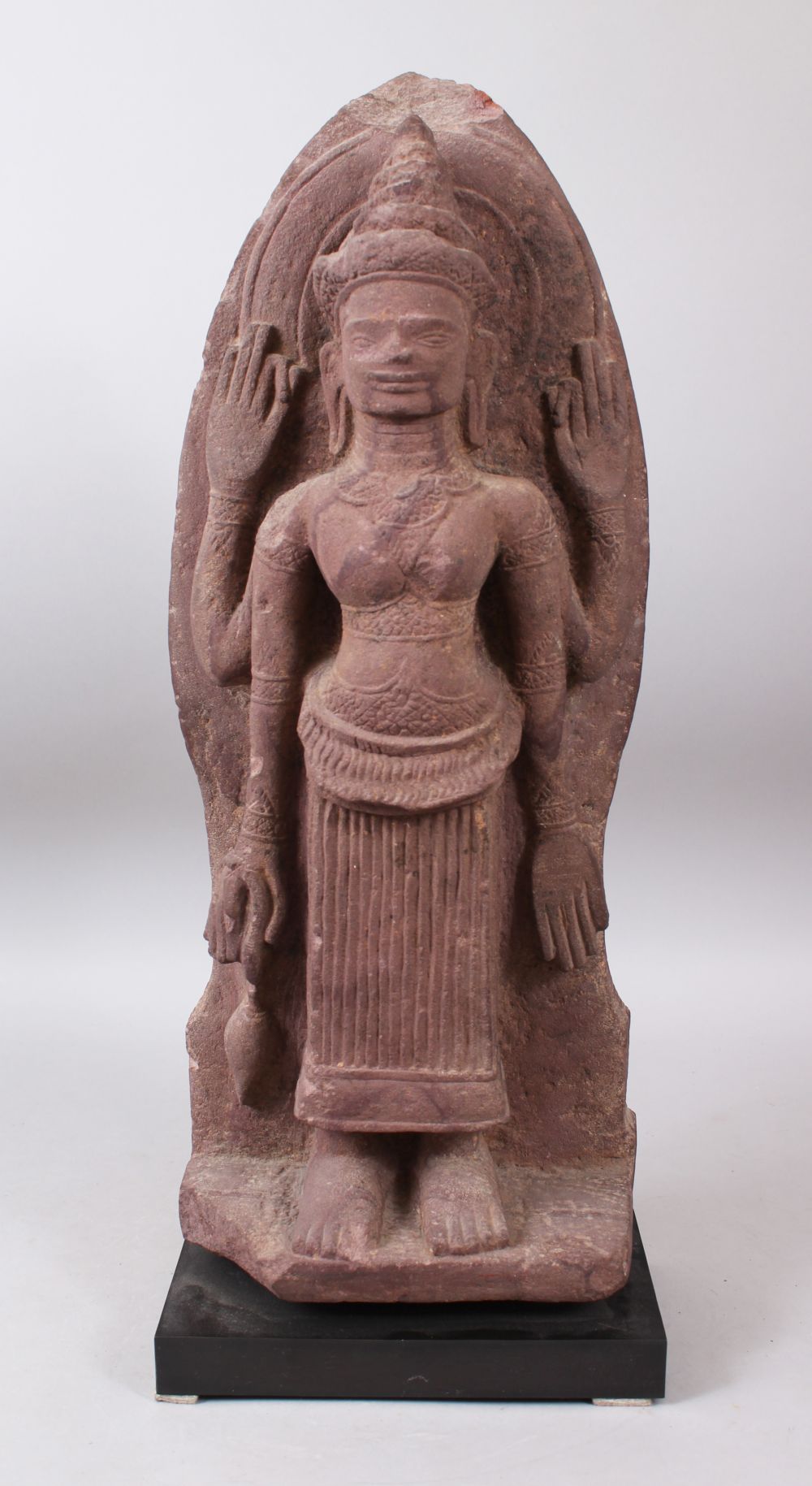 A 12TH CENTURY STYLE CAMBODIAN KHMER STYLE RED SANDSTONE CARVING OF A FOUR ARMED DEITY. 52cms high.