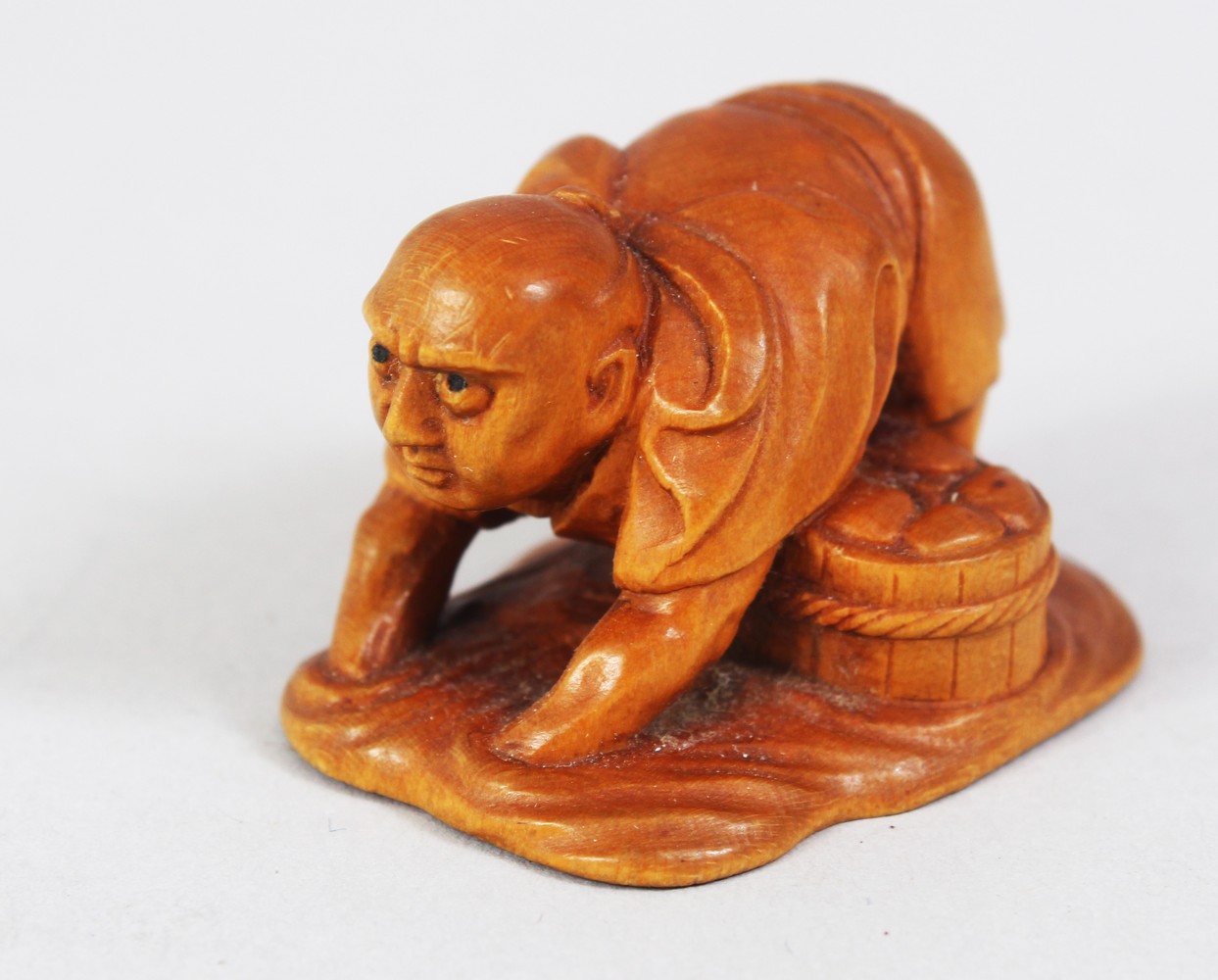 A JAPANESE MEIJI PERIOD CARVED BOXWOOD NETSUKE OF A CLAM FISHERMAN, stood knee deep in water feeling