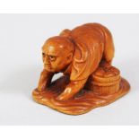A JAPANESE MEIJI PERIOD CARVED BOXWOOD NETSUKE OF A CLAM FISHERMAN, stood knee deep in water feeling