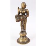 AN 18TH CENTURY INDIAN BRONZE OIL LAMP FIGURE OF LAKSHMI, stood on plinth holding a dish, 27cm