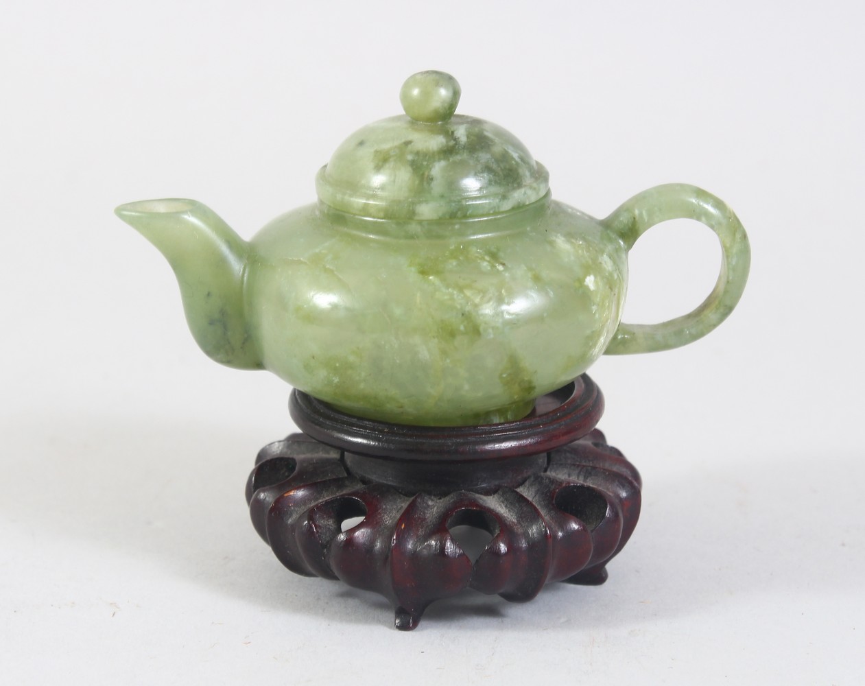 A CHINESE MOTTLED GREEN JADE TEA POT ON PIERCED AND CARVED STAND, 10cm wide.