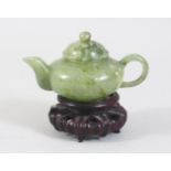 A CHINESE MOTTLED GREEN JADE TEA POT ON PIERCED AND CARVED STAND, 10cm wide.