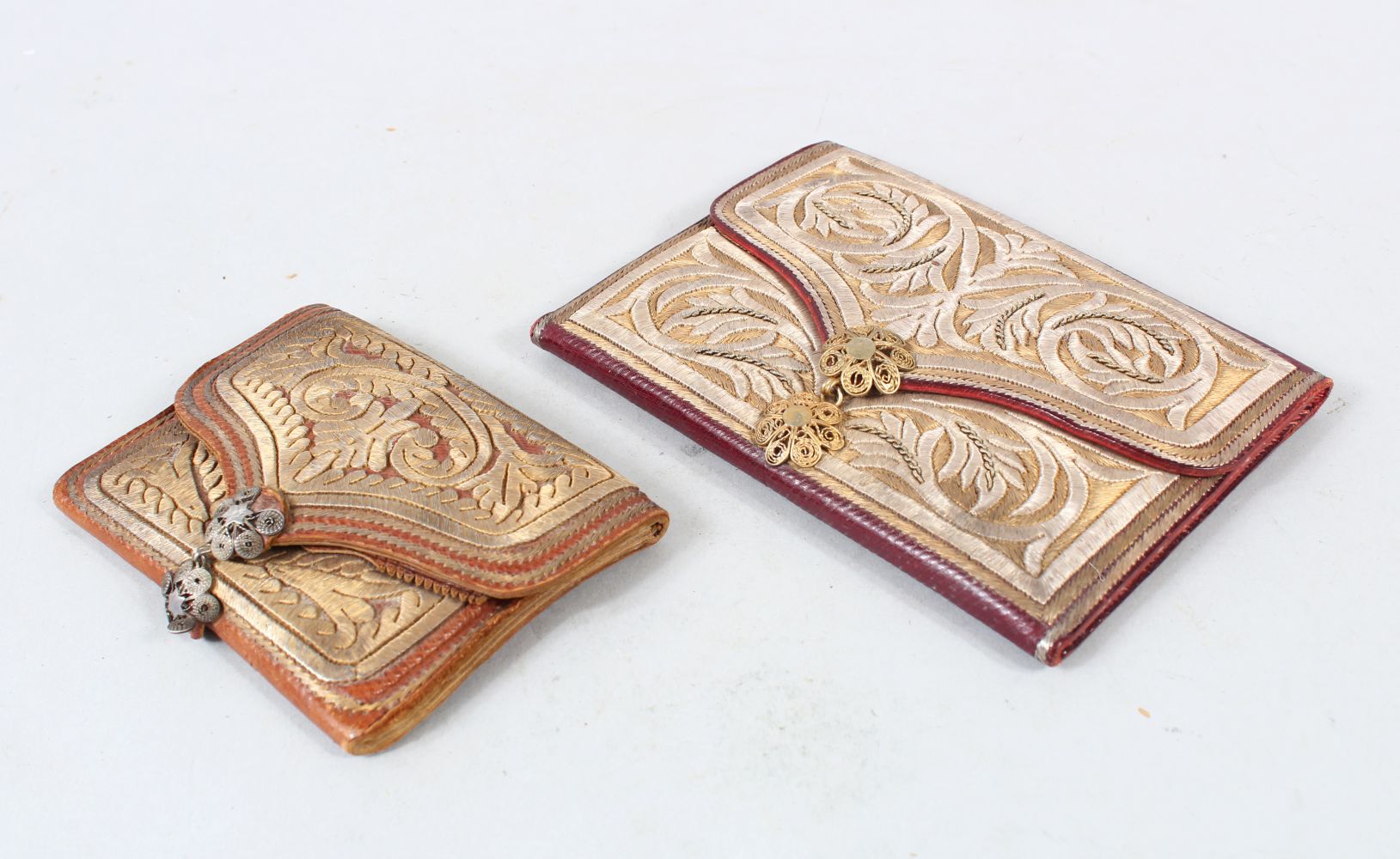 TWO OTTOMAN SILVER THREAD DECORATED LEATHER WALLETS, one dated 1908, 14cm and 10cm wide, (2).