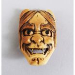 A JAPANESE MEIJI PERIOD CARVED IVORY NETSUKE OF A NOH MASK, the mask with inlaid eyes, and an
