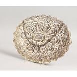 A GOOD CHINESE WHITE METAL MIRROR, of shaped oval outline, embossed with flowers and scrollwork,