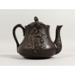 A BROWN GLAZED TERRACOTTA TEAPOT, with moulded decoration. 7ins wide.