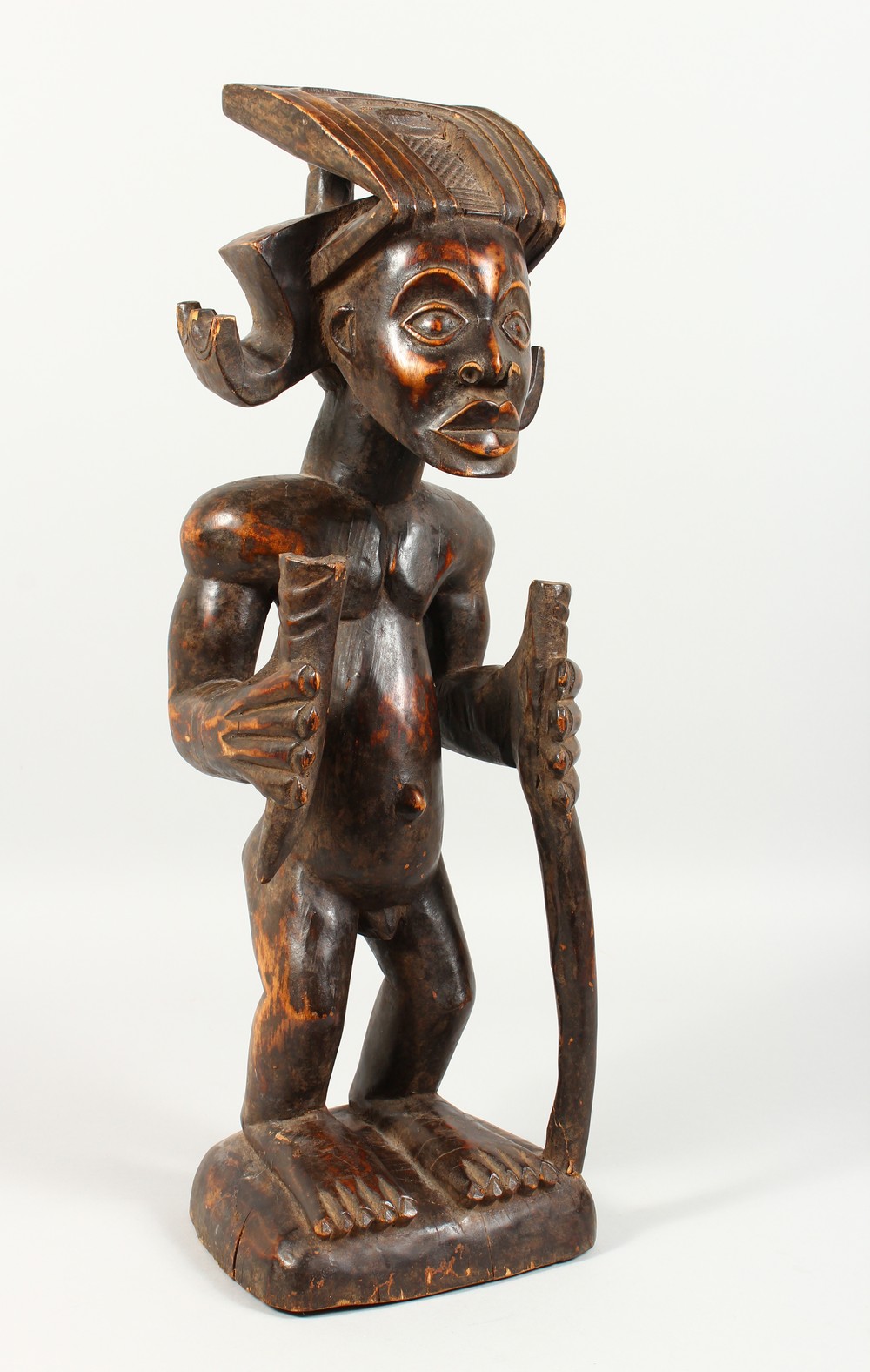 A CARVED WOOD TRIBAL STANDING FIGURE, of a man with headdress, holding a staff. 23ins high.