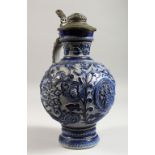 A CONTINENTAL STONEWARE JUG, with blue glazed, moulded decoration and pewter lid. 13ins high.