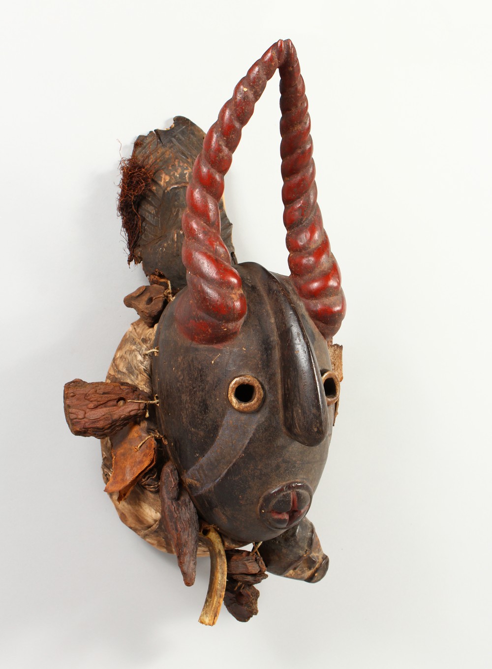 A GOOD CARVED AND PAINTED WOOD MASK, with red painted horns, and symbolic devices hung around the