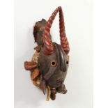 A GOOD CARVED AND PAINTED WOOD MASK, with red painted horns, and symbolic devices hung around the
