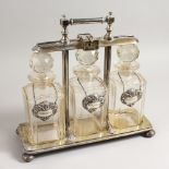 A GOOD LATE VICTORIAN TANTALUS, with patent hinged locking bar, the three cut glass decanters with