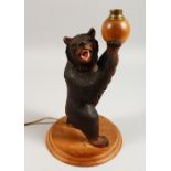 A BLACK FOREST AND CARVED WOOD STANDING BEAR LAMP, on a circular wooden base. 13ins high.