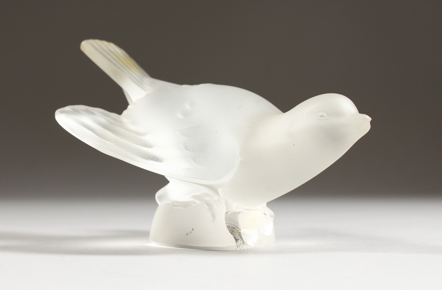 A LALIQUE FROSTED GLASS MODEL OF A BIRD, wings outswept, (base chipped). 5ins long.