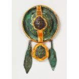 A ROMAN BRONZE AND GILT PENDANT, set with two masks, set as a brooch. 5ins long x 2.75ins diameter.