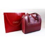 A CARTIER MAROON LEATHER BAG in a Cartier bag.