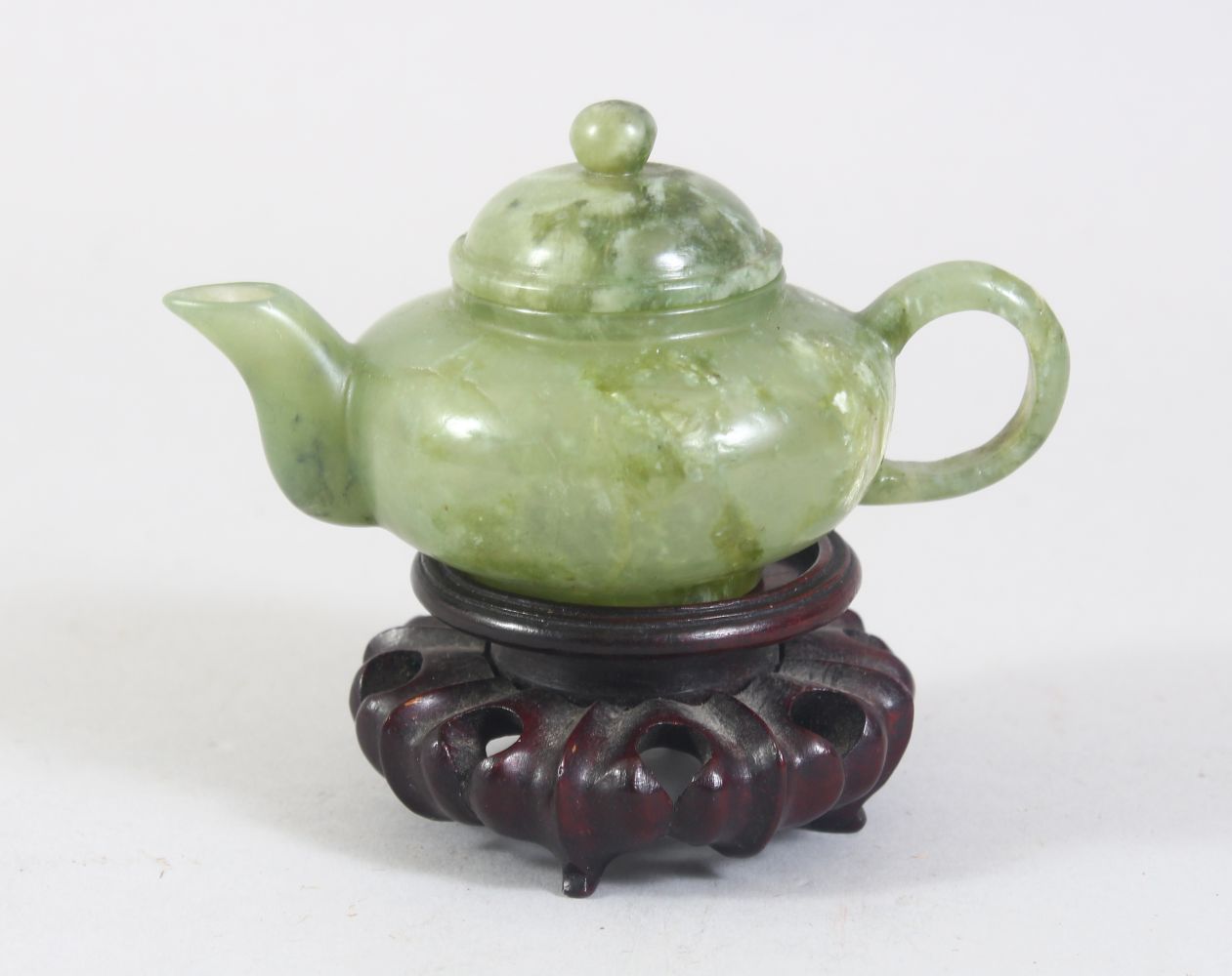 A CHINESE MOTTLED GREEN JADE TEA POT ON PIERCED AND CARVED STAND, 10cm wide.