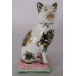 Mid 19th century Staffordshire pottery figure of a cat wearing a gilt bow and seated on a cushion. H