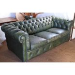A three-seat chesterfield settee, button upholstered in a green leather, on bun feet, 74" wide