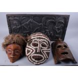 An African mask made from natural materials, two wooden carved masks and a carved wooden plaque