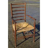 A Gimson design ladder back elbow chair with rush envelope seat, on turned and stretchered supports