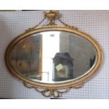 An oval gilt framed bevelled edge wall mirror with vase and swag crest, 36" wide
