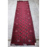 A Pakistan Bokhara runner with thirty-four octagonal guls on a deep red ground, 104" x 35" approx