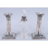 A pair of silver filled pillar candlesticks, on square bases, and a silver mounted toilet bottle