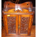 A smoker's late Victorian carved oak cupboard with fitted interior enclosed two floral panelled