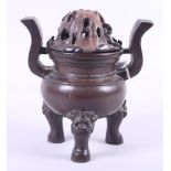 A Chinese bronze two-handled censer, on three feet decorated lion masks, with matched wooden lid