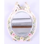 A Continental porcelain framed oval mirror, decorated with flowers and two cherubs