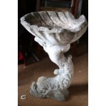 A cast stone bird bath, formed as a dolphin with a shell on its tail