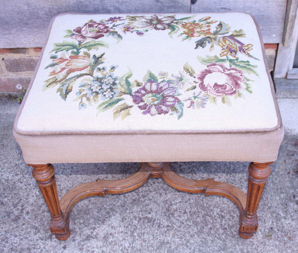 A carved walnut stool of Louis XVI design with needlepoint seat, on square taper supports united