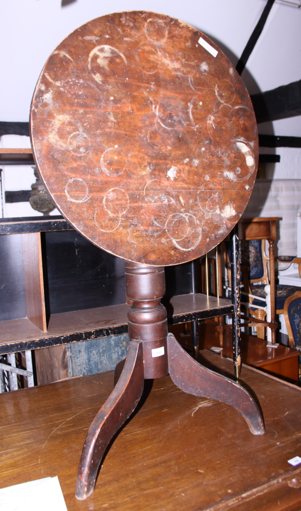 An early 20th century oak tilt top circular table, on three splayed supports (heavy staining to