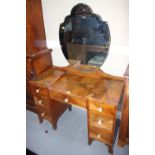 A 1930s figured walnut drop centre dressing table with shaped mirror over seven drawers, on