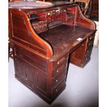A polished as mahogany roll top desk with tambour shutter enclosing drawers and pigeonholes, on