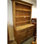 A stripped pine dresser, the upper section with open shelves over three drawer and cupboards