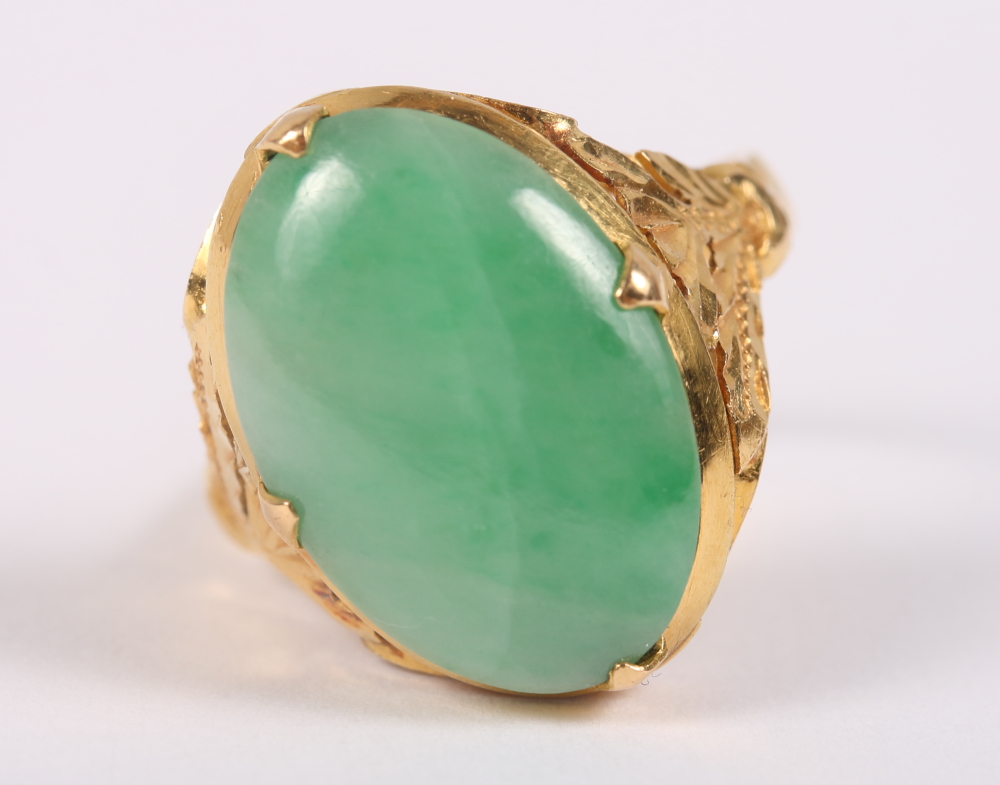 An early 20th century yellow metal jade cabochon ring with floral decoration to shoulders, ring size