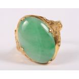 An early 20th century yellow metal jade cabochon ring with floral decoration to shoulders, ring size