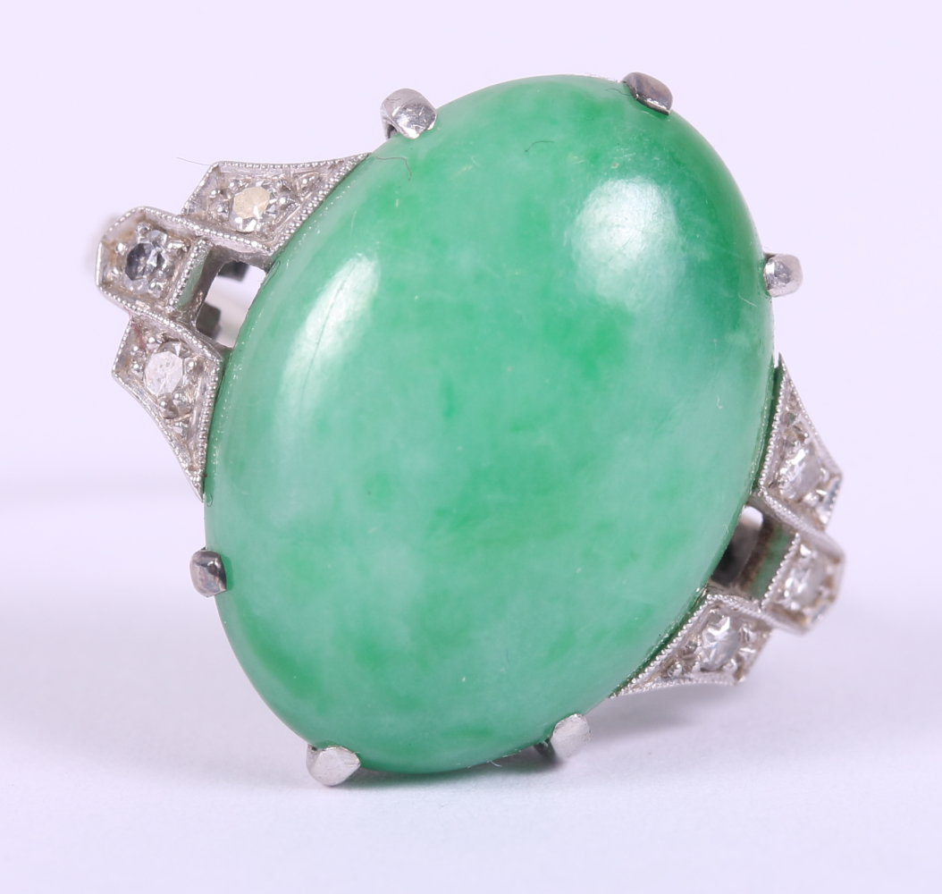 An Art Deco white metal ring, set jade cabochon, flanked three diamonds to each shoulder, ring