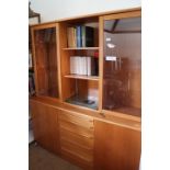 A teak wall unit, fitted two glazed doors over cupboards flanking five graduated drawers, 64" wide